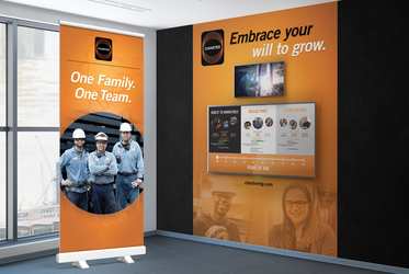 Room with Charter banner-up "One Family. One Team" and wall featuring video monitor and touch-screen interactive monitor below "Embrace your will to grow" headline