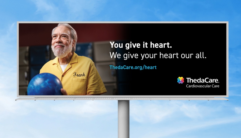 Billboard showing an older man in a bowling shirt holding a bowling ball with headline about giving your heart and ThedaCare cardiovascular care branding.