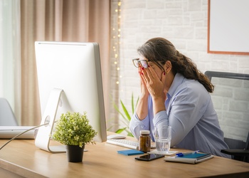 women sitting at computer desk rubbing her eyes from frustration