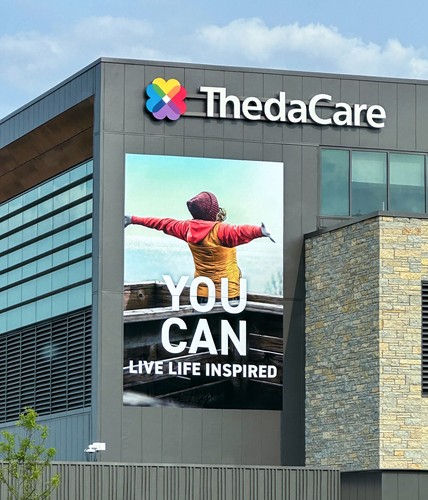 Exterior of ThedaCare building with large graphic of woman with arms spread out with the words "YOU CAN LIVE LIFE INSPIRED"