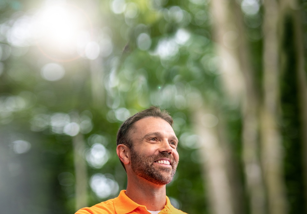 A man standing in nature surrounded by trees and sunlight