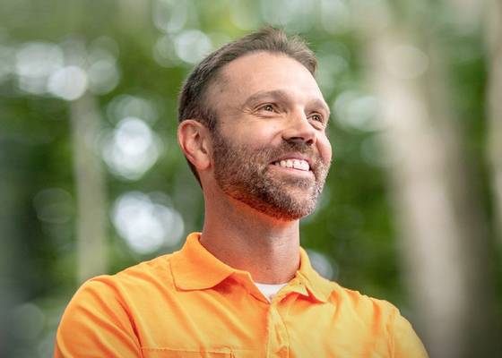 A man standing in nature surrounded by trees and sunlight