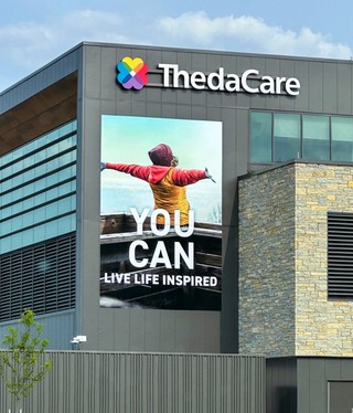 Exterior of ThedaCare building with large graphic of woman with arms spread out with the words "YOU CAN LIVE LIFE INSPIRED"