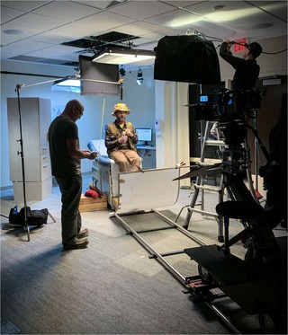 Shooting a scene for a commercial with director in foreground and actor in background under lights.