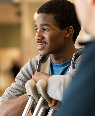 A scene from a TriHealth ad where a young man with crutches is smiling.